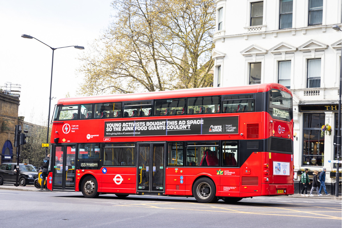 A red London bus driving down a busy London road, it has the Bite Back advert on the side. The advert reads Young Activists Bought This Ad Space So The Junk Food Giants Couldn't. We're Giving Kids A hashtag Commercial Break