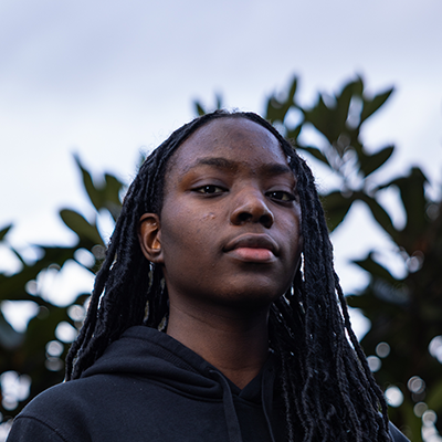 A young black woman with her hair pushed back is looking into the camera with a serious gaze.