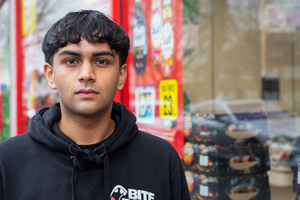 Bite Back activist Dev stands outside a high street supermarket, he is looking at the camera with a serious expression