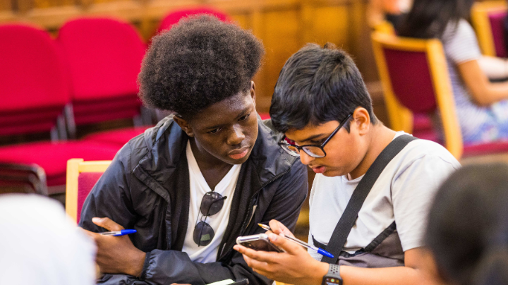Bite Back activist Farid is sitting with another activist Rizwan, Rizwan is holding a phone and they are both looking at the screen