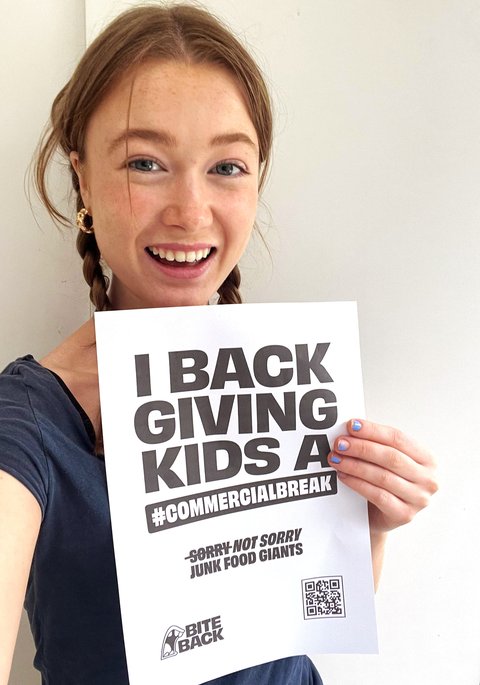 Clemmie holding up commercial break poster and smiling (edited)