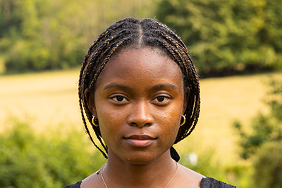 A young black woman with braids pulled back into a ponytail is looking in the camera with a powerful stare.