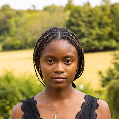 A young black woman with braids pulled back into a ponytail is looking in the camera with a powerful stare.