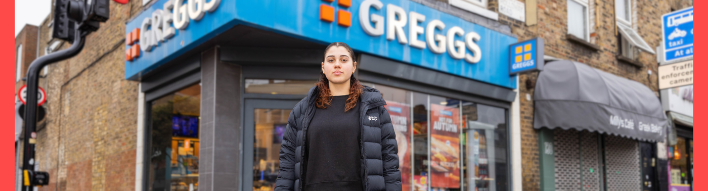 Young woman standing in front of a Greggs bakery on a city street