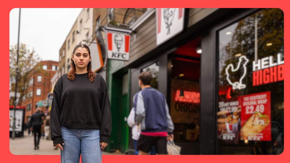 A young woman stands on a busy city sidewalk in front of a KFC restaurant. She wears a black sweatshirt and jeans, looking at the camera while pedestrians pass by and the KFC sign and posters appear behind her.