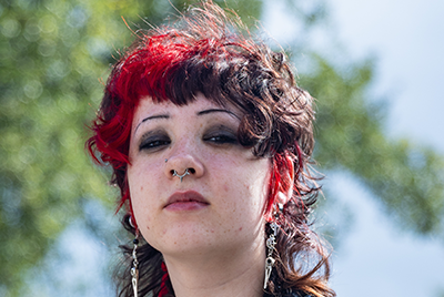 A young person with dyed red and black hair is looking powerfully into the camera