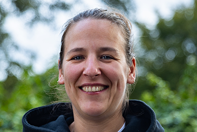 Rachel is a young white woman with long brown hair wearing a white shirt in front of a background of sunsoaked fields.