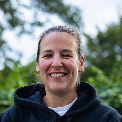 Rachel is a young white woman with long brown hair wearing a white shirt in front of a background of sunsoaked fields.