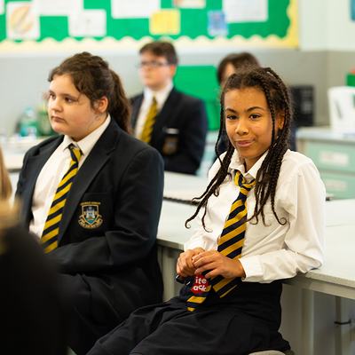 A young student wearing school uniform leans against a desk.
