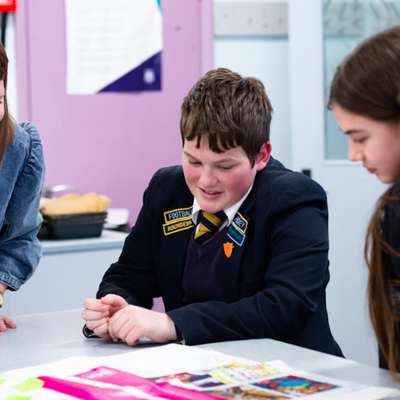 Three school students and an adult sit around a classroom table taking part in a Bite Back in Schools activity, they are all smiling