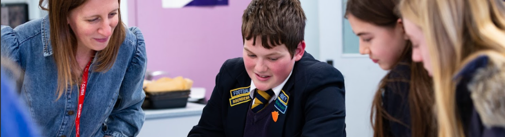 Three students sit around a classroom table with an adult, they are smiling and taking part in an activity