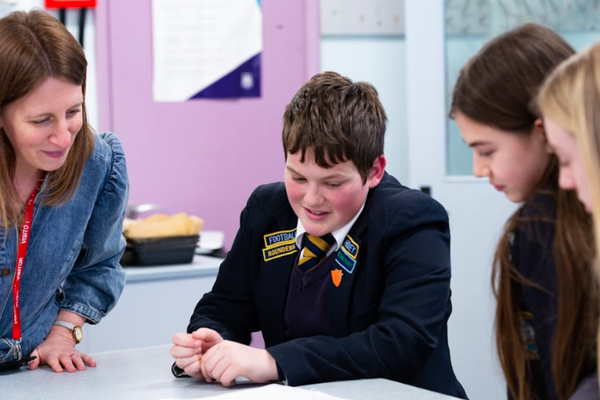 Three students sit around a classroom table with an adult, they are smiling and taking part in an activity