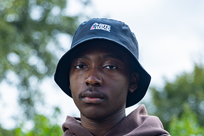 A young black man wearing a bucket hat is staring into the camera with a powerful expression.