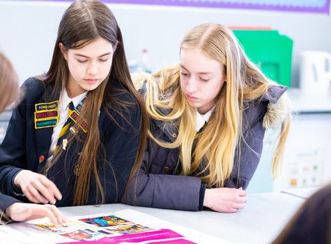 Two girls in school uniform look at a sheet of paper on a table, taking part in a Bite Back in Schools session.
