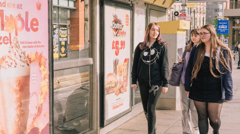 Lucy, Brooke and Ollie walking along a bus stop in Manchester
