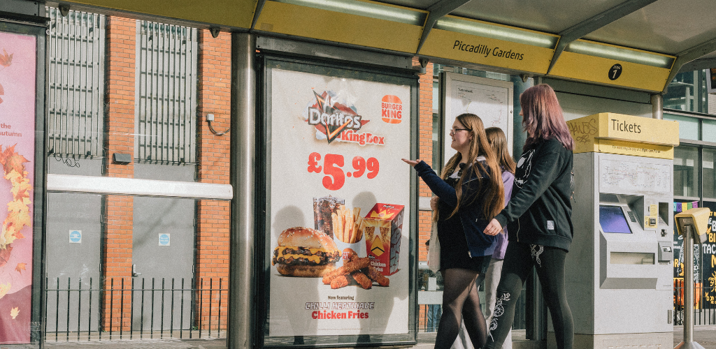 Three Bite Back activists are looking at a junk food advert at a bus stop in Manchester.