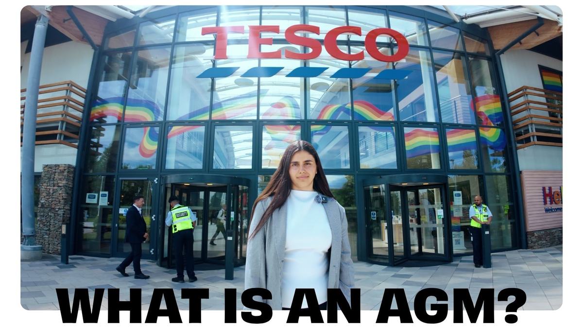 Front view of a Tesco entrance with a glass facade and rainbow window graphics. A woman stands in the foreground while security staff and other people move near the revolving doors. Bold partial text "WHAT IS AN AGM?" appears at the bottom.