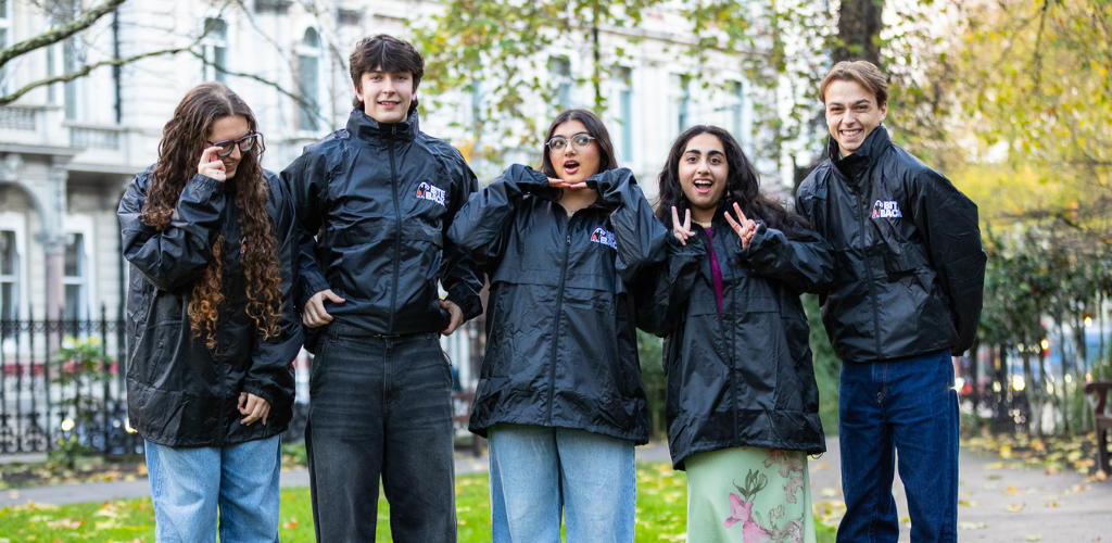 A group of young people wearing black Bite Back jackets are stood on a patch of grass, smiling together.