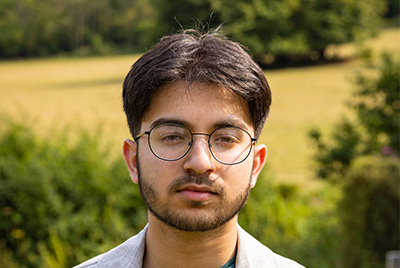 A young man with cropped brown hair and black glasses is looking straight on into the camera.