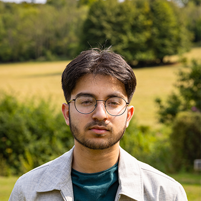 A young man with cropped brown hair and black glasses is looking straight on into the camera.