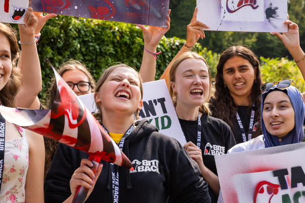 A group of young people are stood in a field smiling and cheering as they hold protest signs.