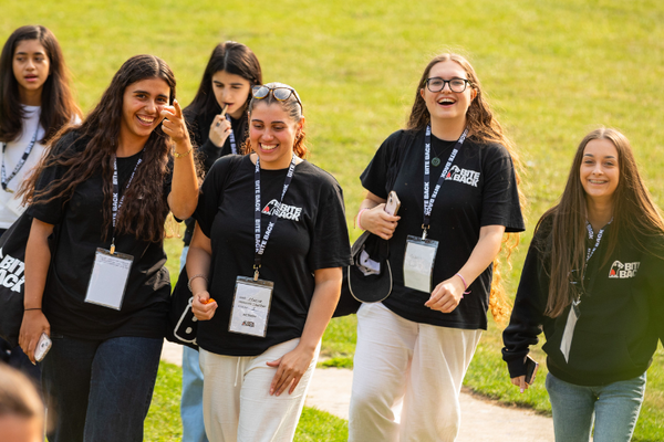 A group of young people are walking on a field, wearing black Bite Back t-shirts and laughing.